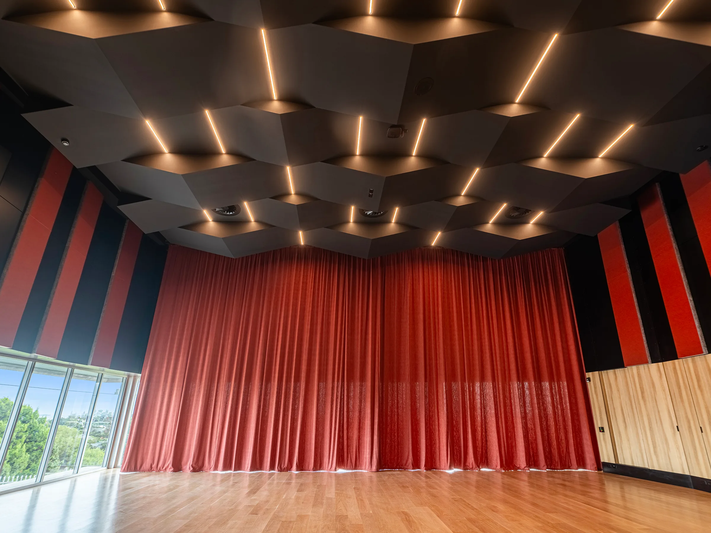 A school performance hall with red drapes and a faceted acoustic ceiling