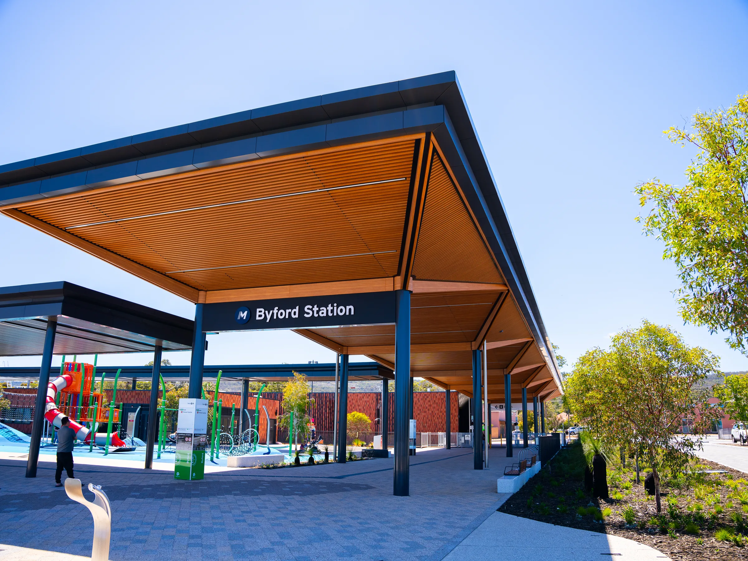 A timber-lined platform canopy folding over blue steel columns
