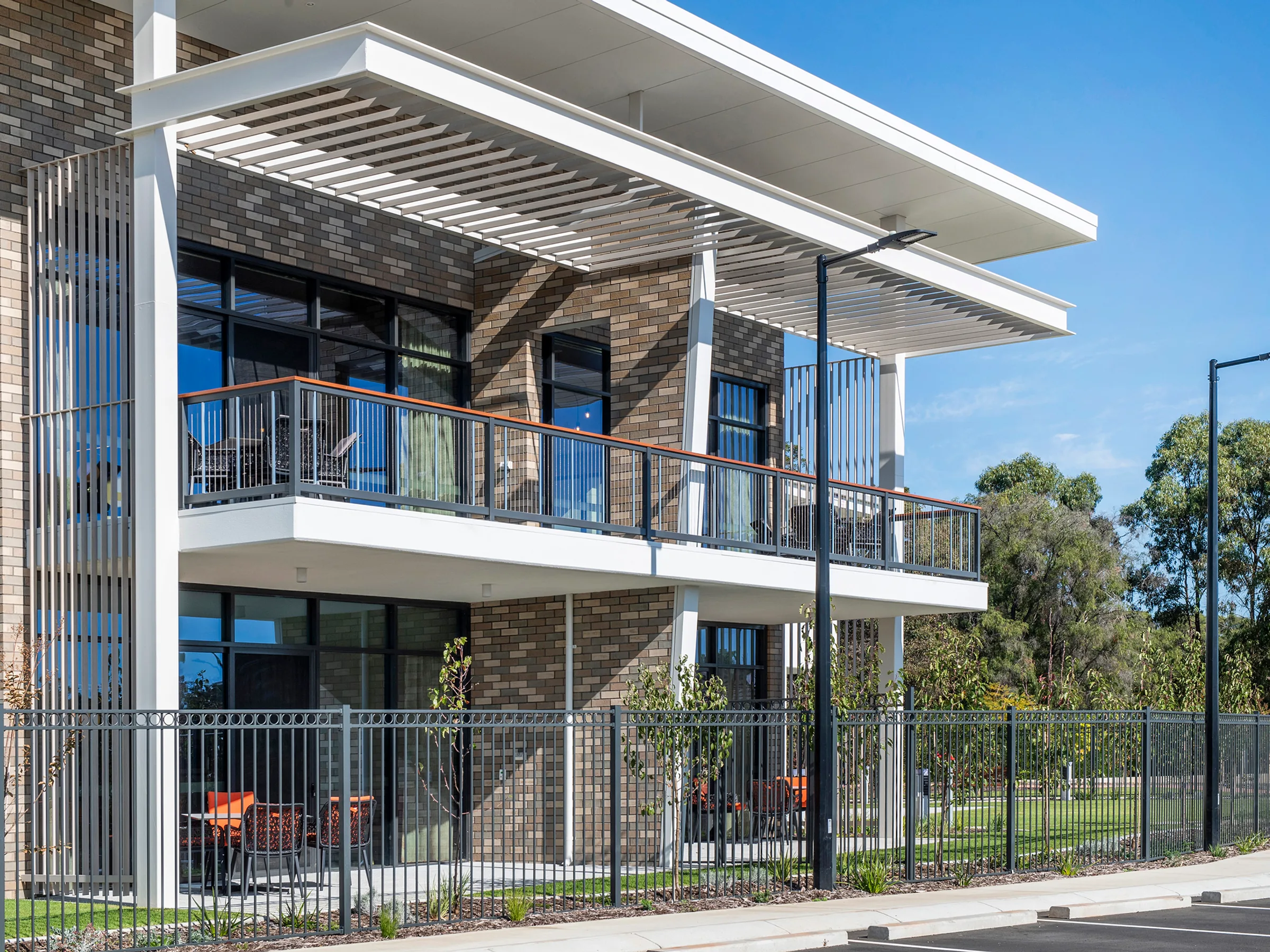 A two-storey brick facade with balconies and timber screening above a landscaped garden