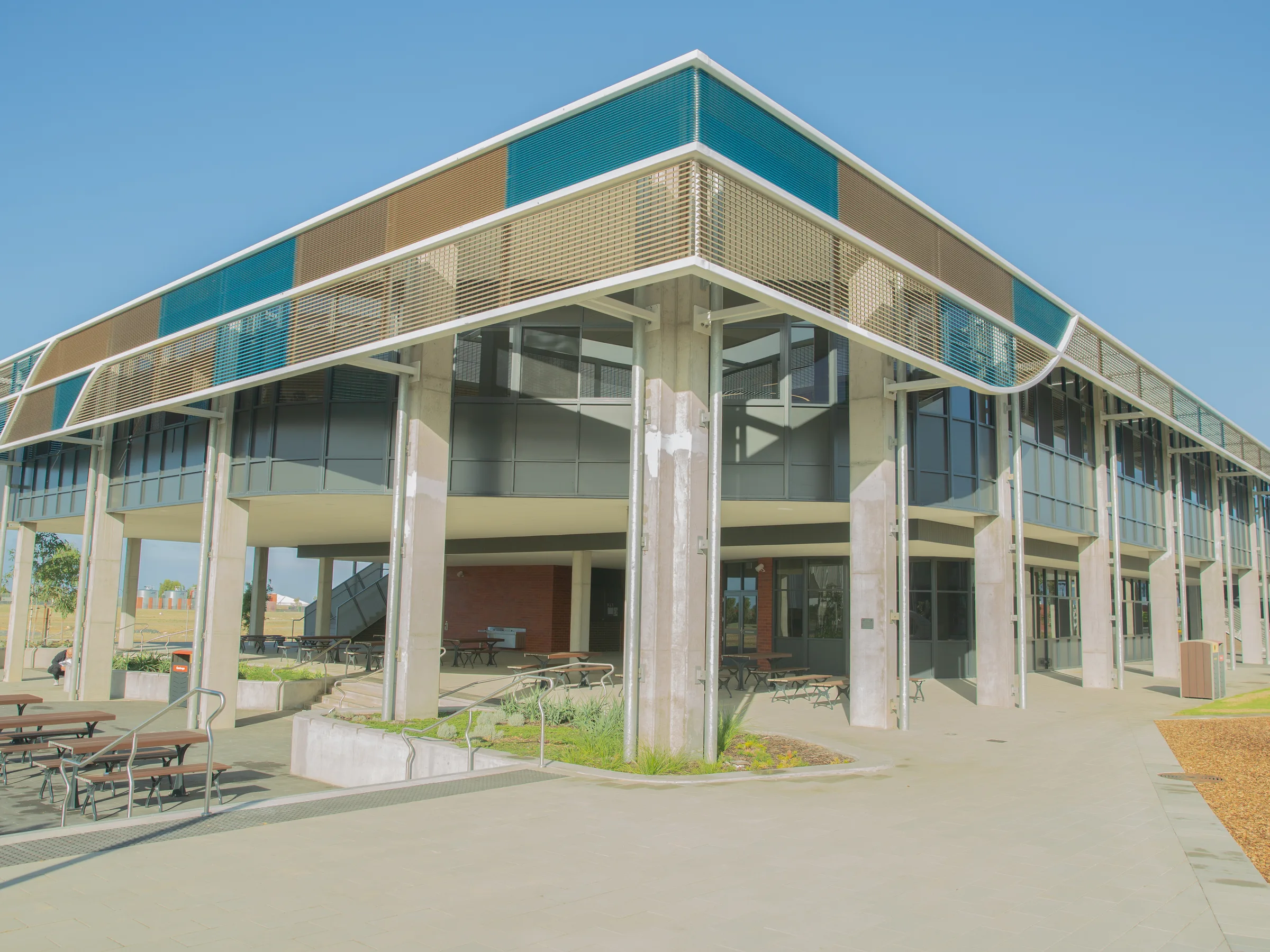 A teal-glazed two-storey college building above a landscaped forecourt