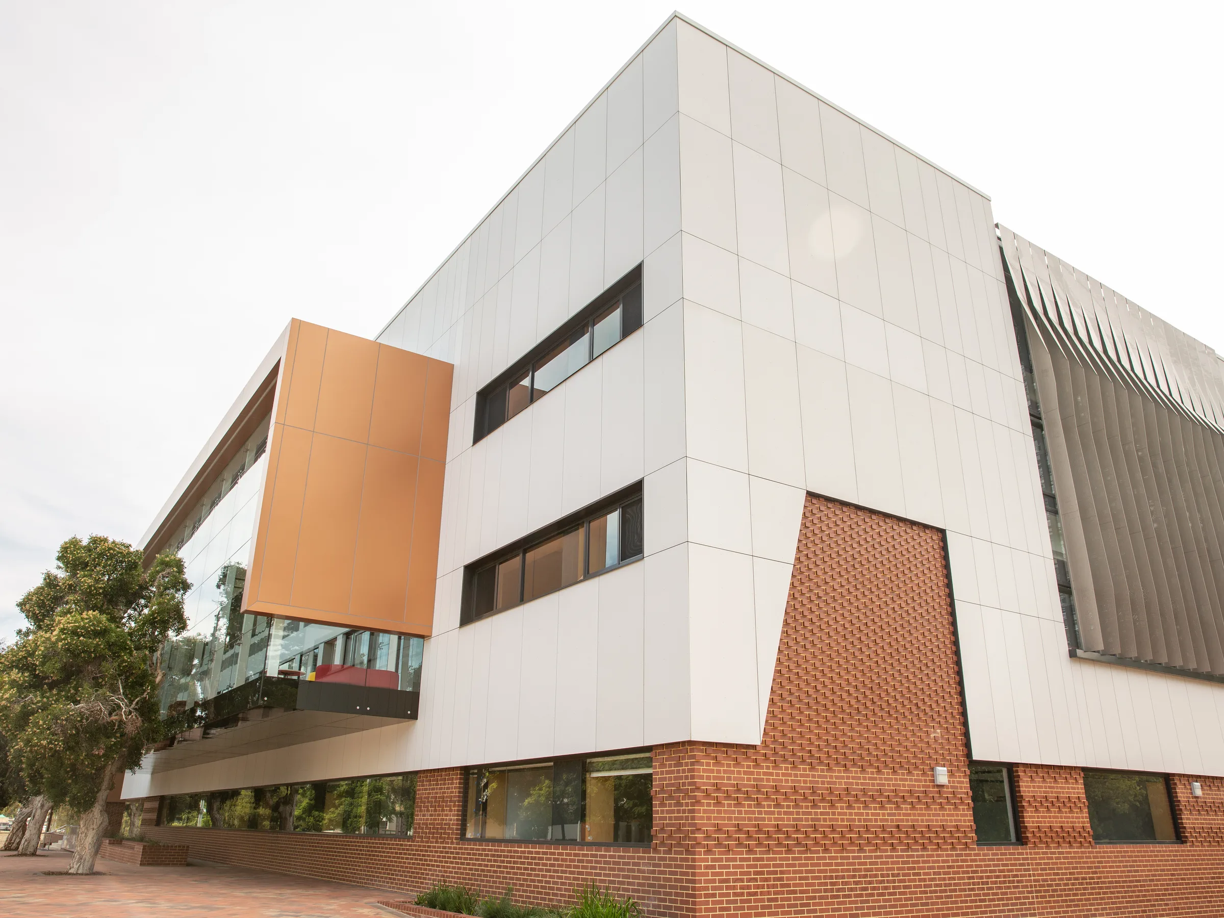 An angular white-panelled college building with an orange soffit above a brick base