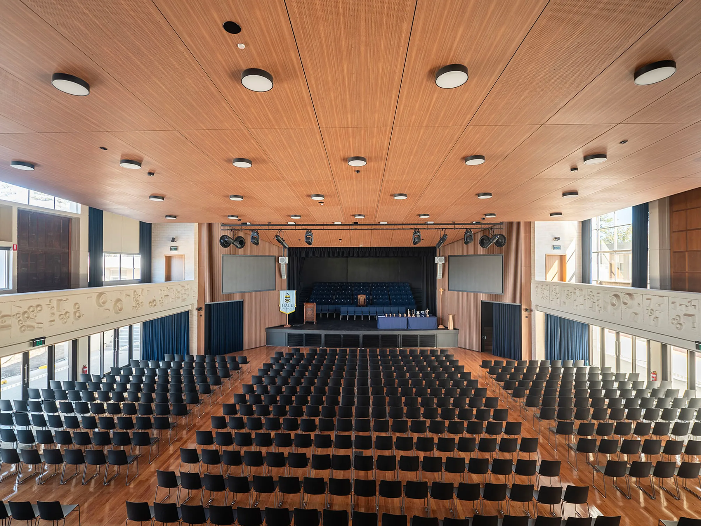 A school auditorium lined with a timber-battened ceiling above tiered seating